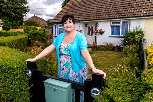 An Eastlight resident standing and smiling in front of her home, leaning against her garden gate.