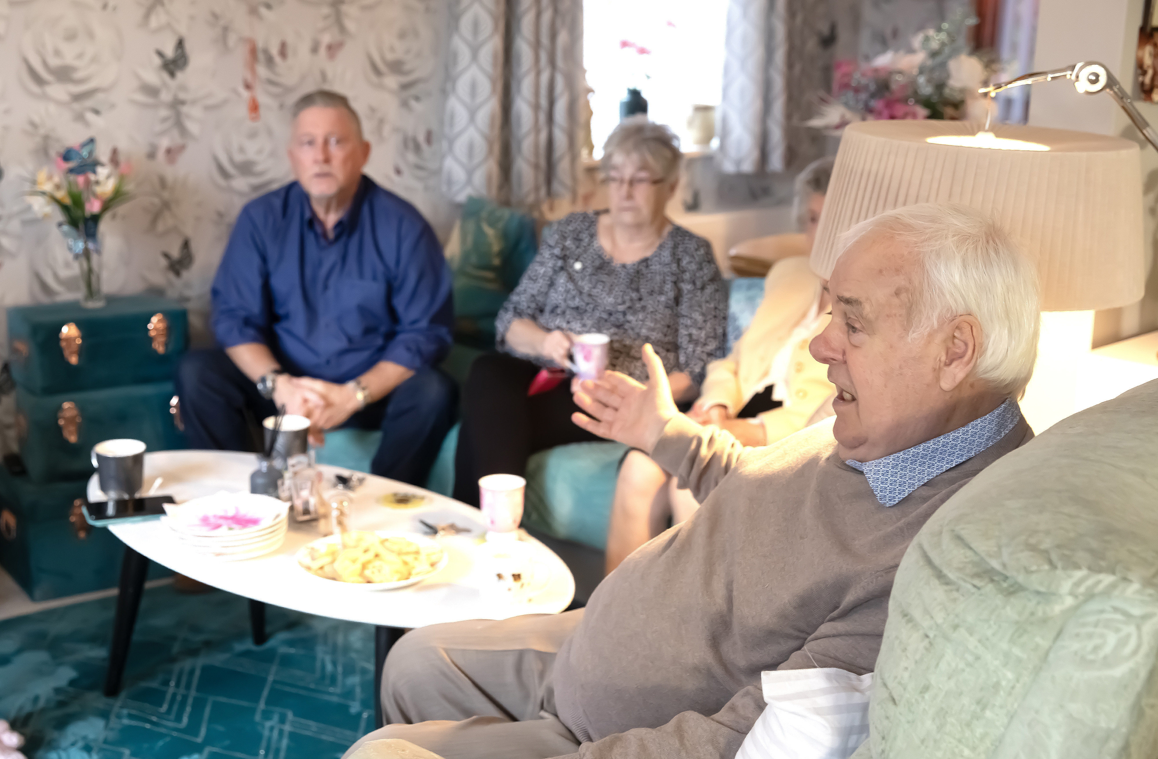 A man and a woman are sat together on a sofa. Another man is sat in an armchair they are all talking.