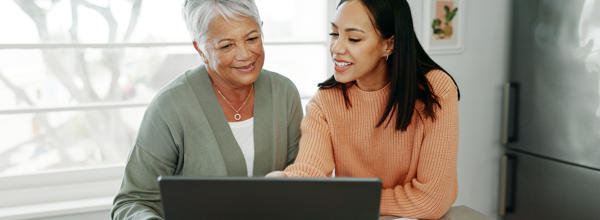 A younger woman is helping an older woman with her finances on a laptop.