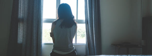 woman sitting on bed in room with light from window