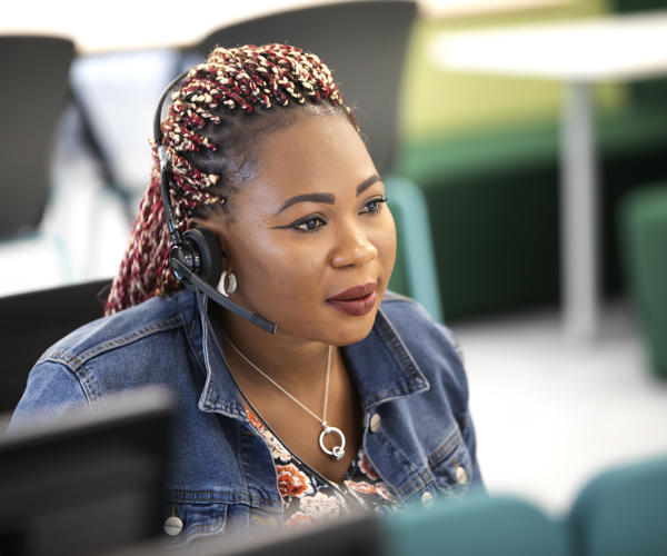 A woman is wearing a headset and looking at a computer screen.