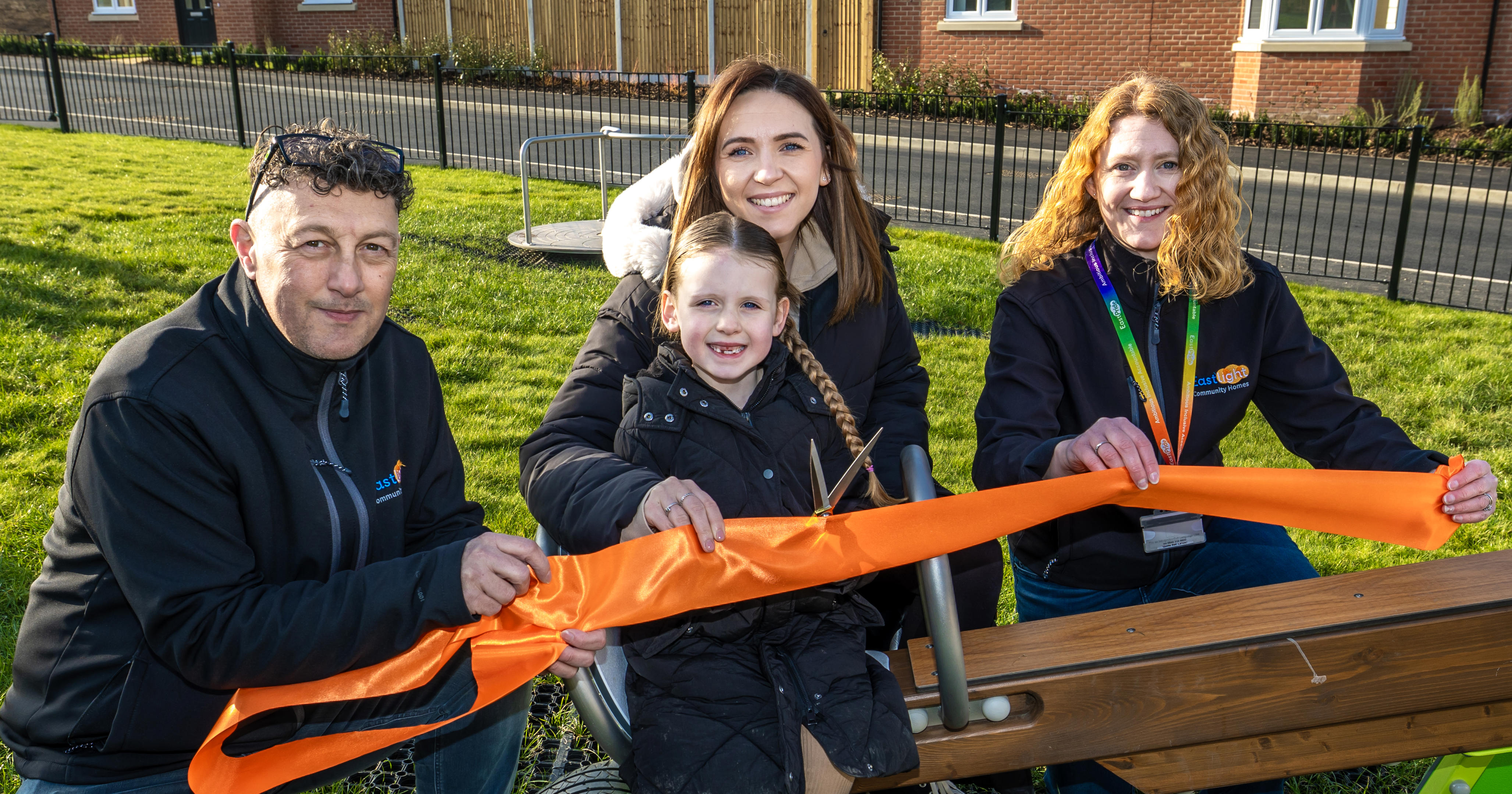Eastlight's Debbie Mitchell and Andy Allocca are with Eastlight family Charlea and her daughter Lilly. They are all holding onto a ribbon while at an event opening the new playground.