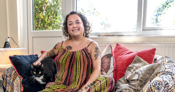 Young resident Bobbie Town is sat on a sofa in her home. Her black and white cat is sat next to her.