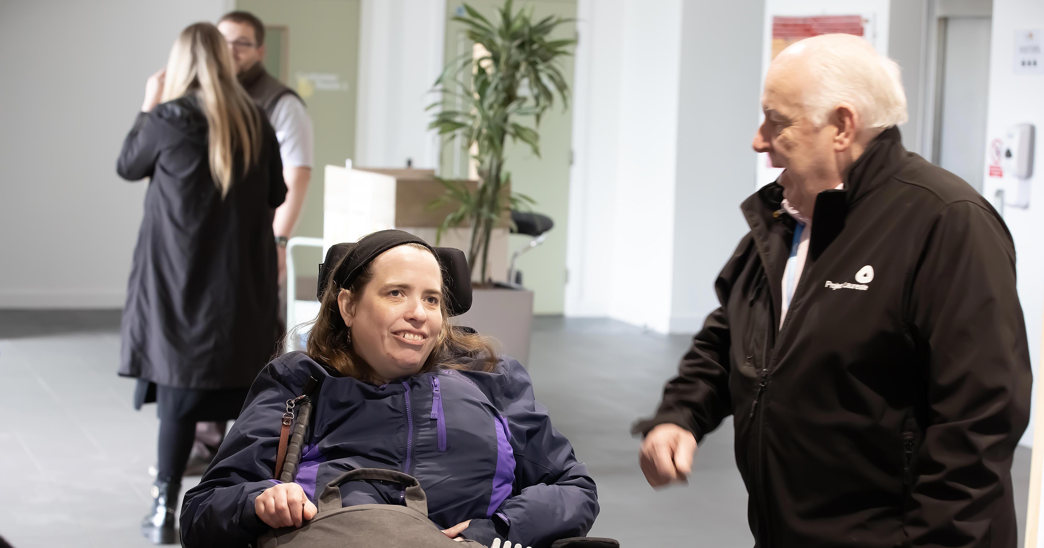 A woman in a wheelchair is speaking to a man stood next to her.