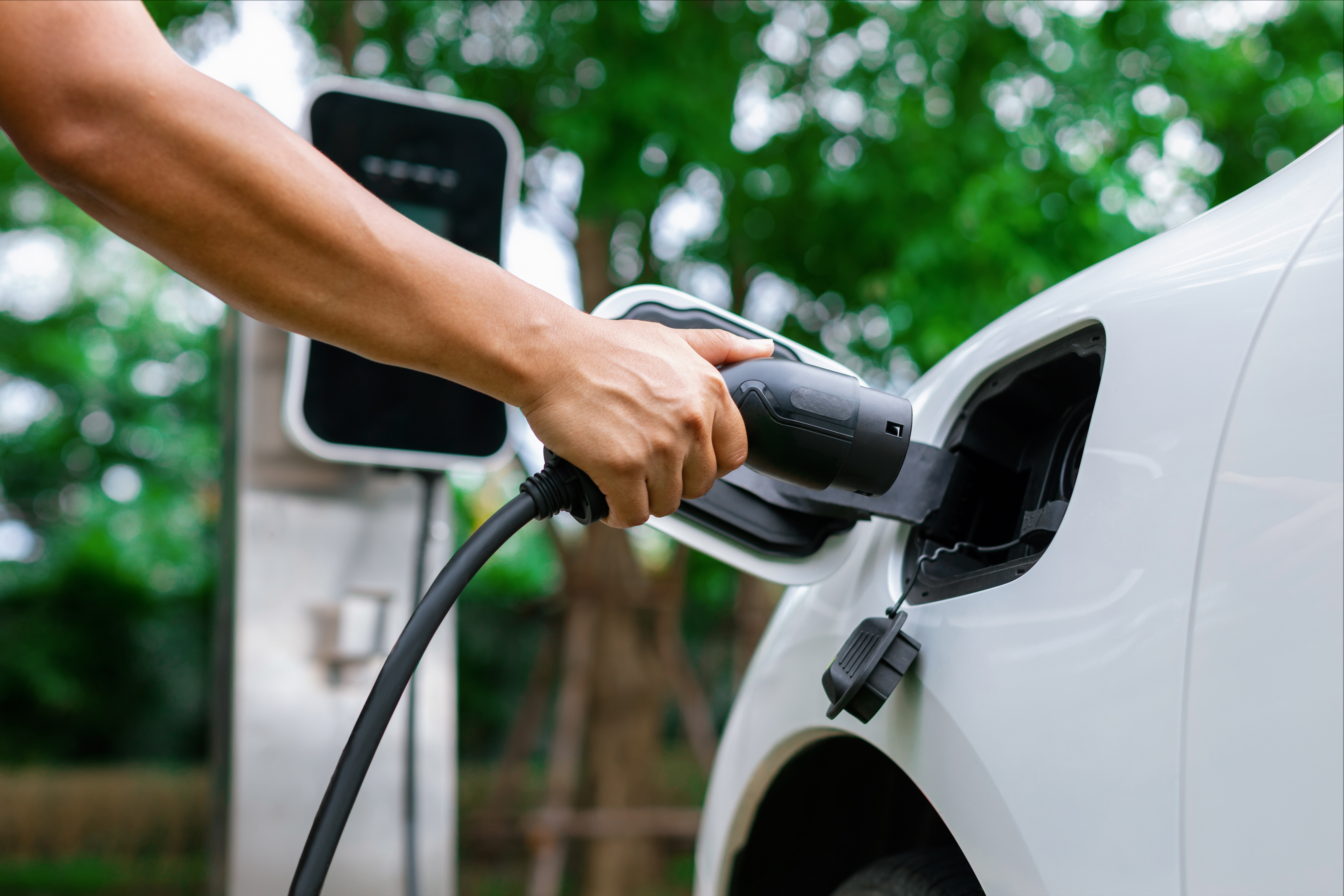 A hand is putting an electric car charger into the car socket.