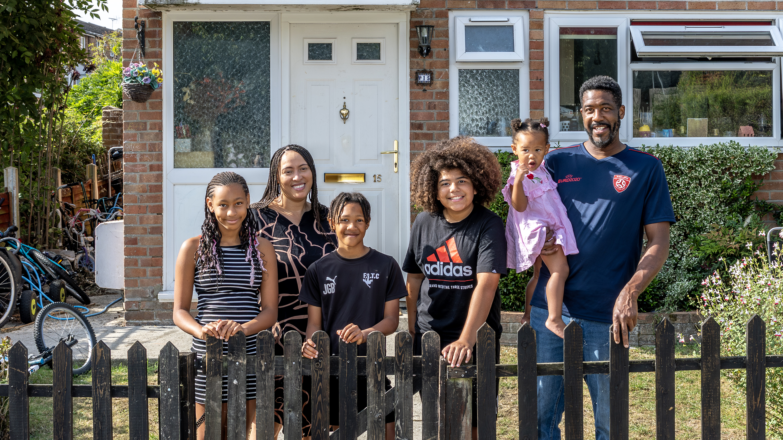 Eastlight resident, Shereen Faure, her partner and four children are stood against a short picket wooden fence at the front of their home.