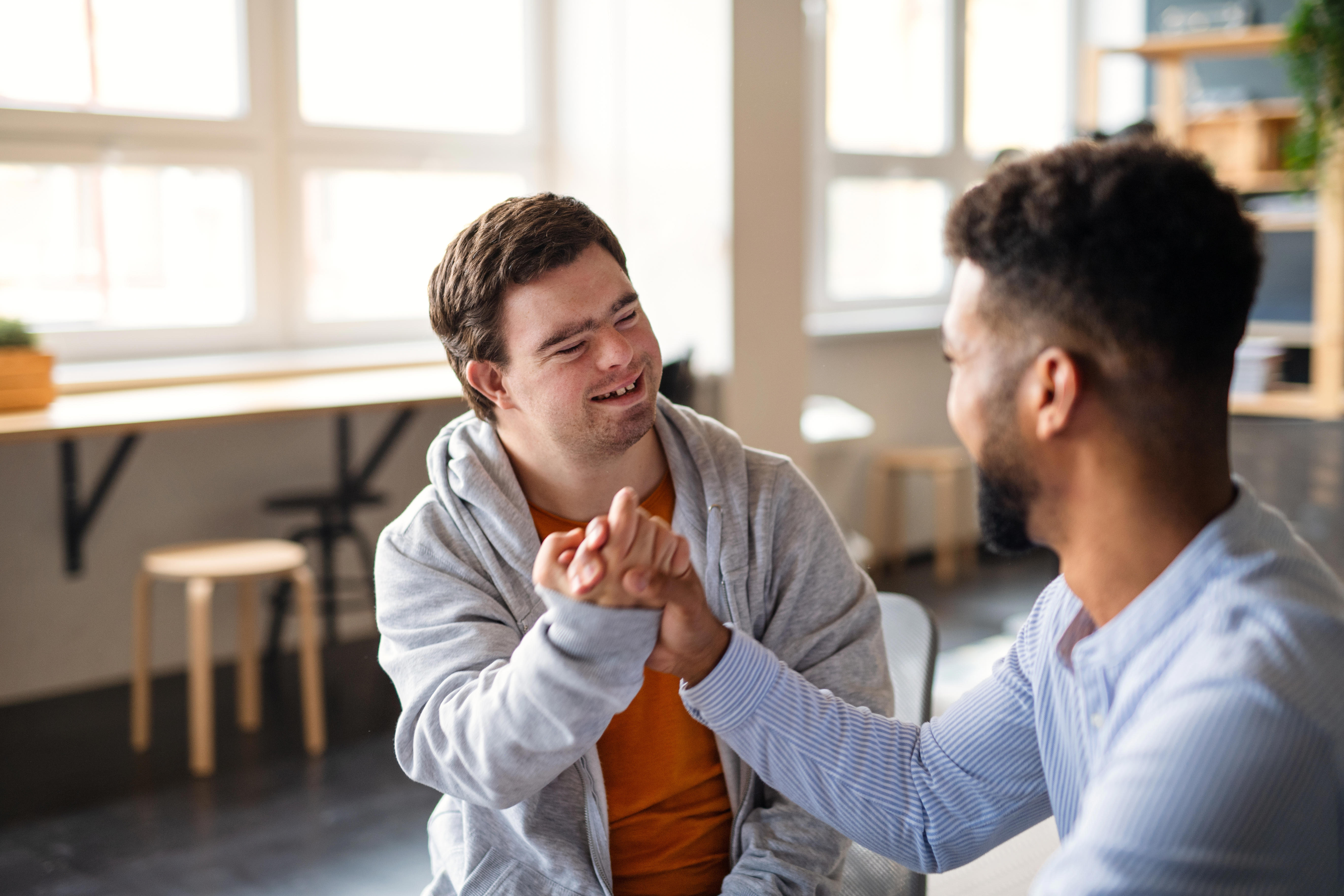 A disabled man is shaking the hand of another man and smiling at him.