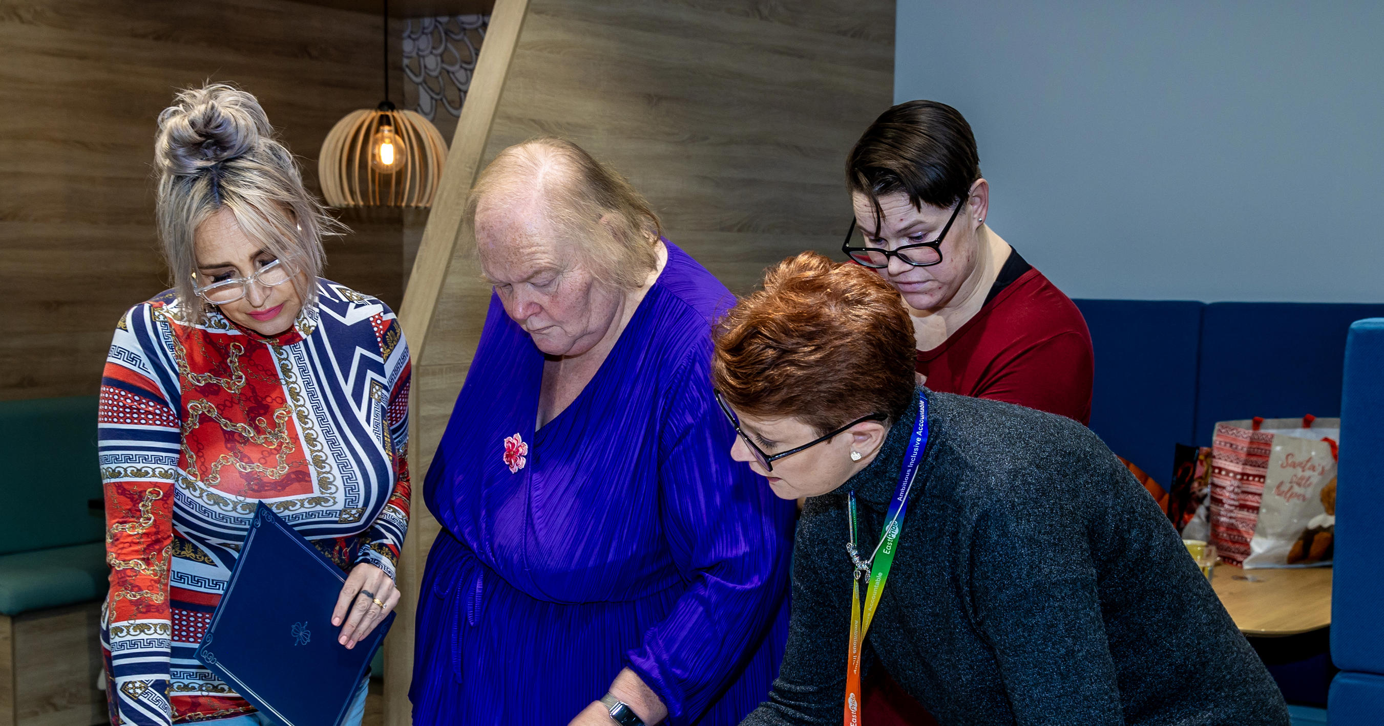 A group of four women are stood around a table looking at big pieces of paper which have been written on.