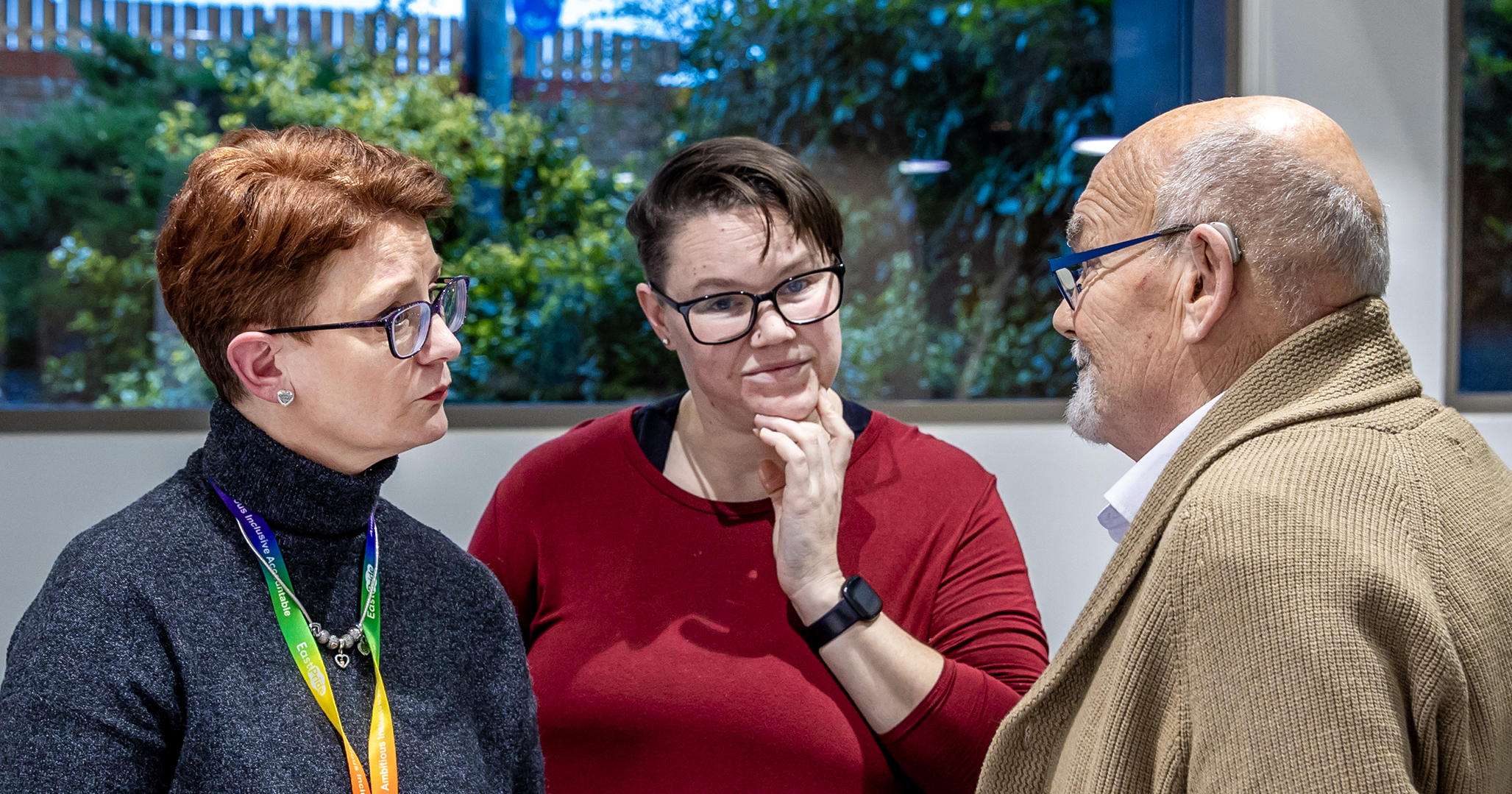 A man and two women are stood together in a group. They are all looking at each other, mid-conversation.