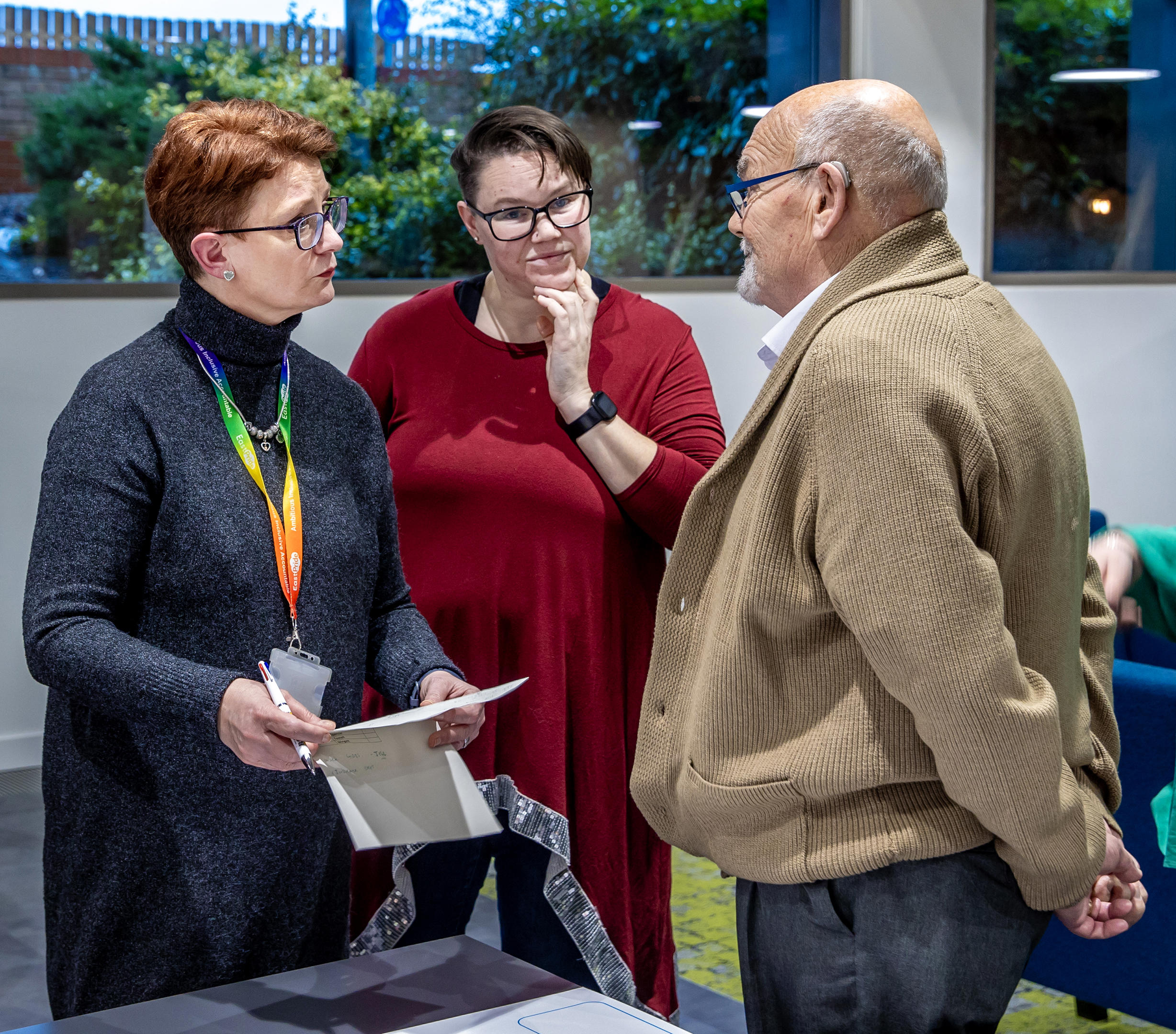 A man and two women are stood together in a group. They are all looking at each other, mid-conversation.