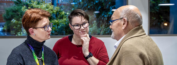 A man and two women are stood together in a group. They are all looking at each other, mid-conversation.