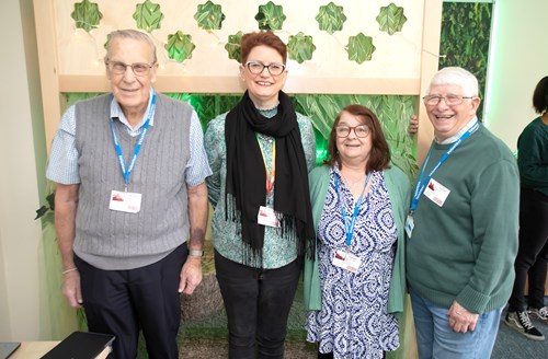 Two women are stood in between two men. They are all smiling at the camera.