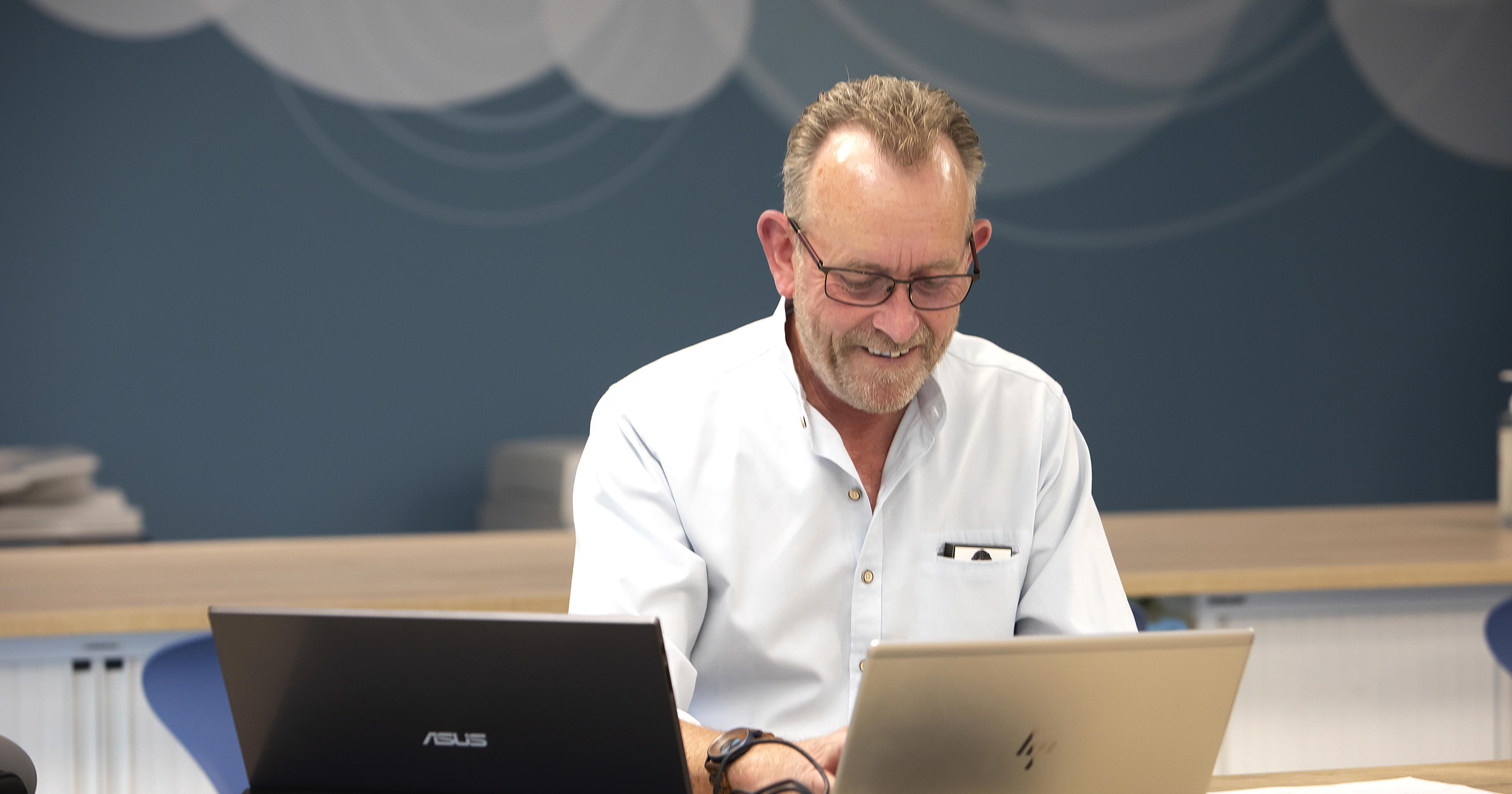 A man wearing a shirt is looking down at his laptop screen.