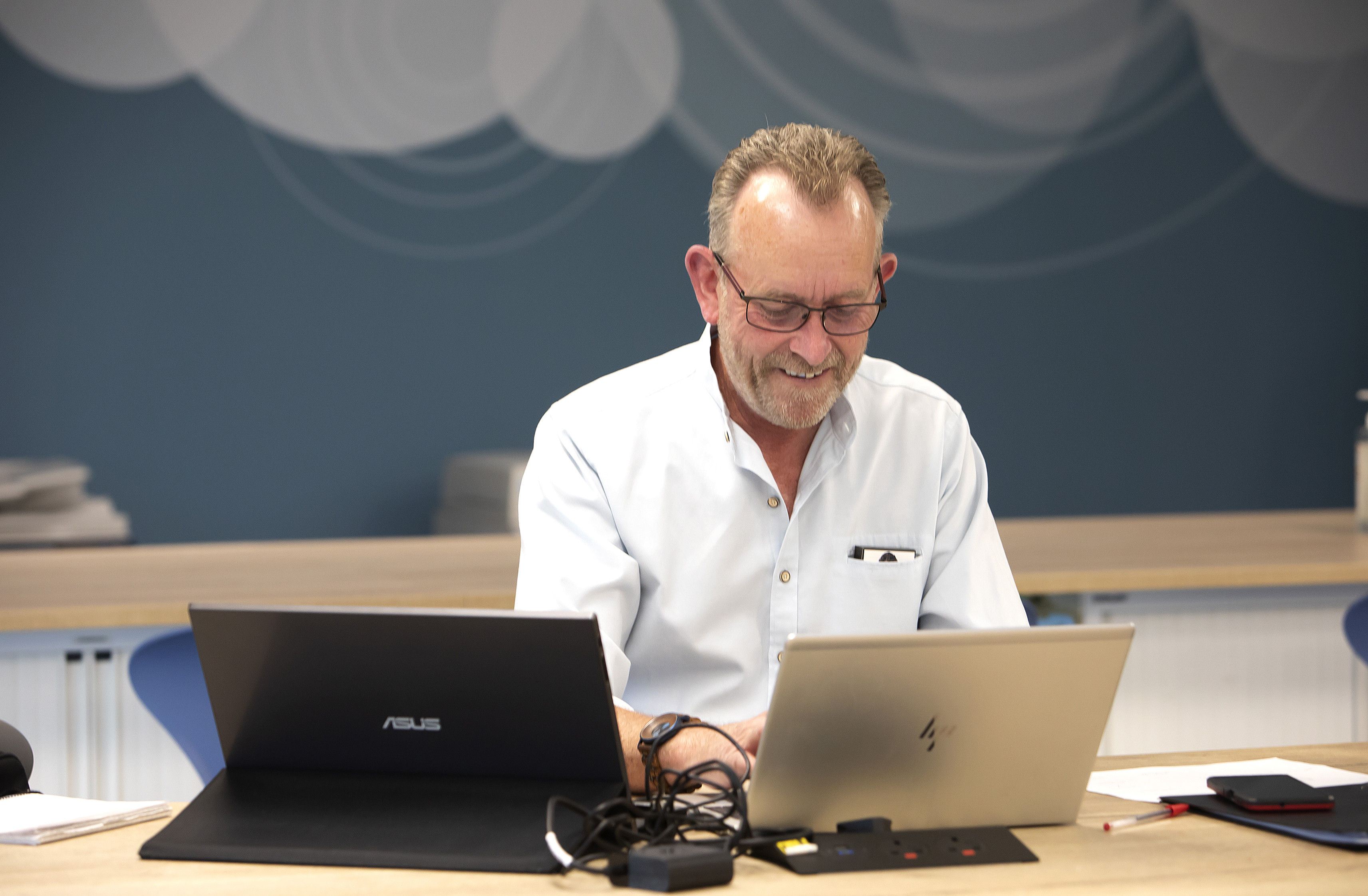 A man wearing a shirt is looking down at his laptop screen.